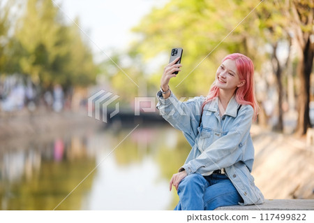A woman with pink hair is taking a selfie with her cell phone A woman with pink hair is taking a selfie with her cell phone 117499822