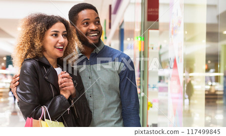 A joyful African American man and woman are strolling through a mall corridor, their expressions suggesting they just made some delightful purchases, copy space 117499845