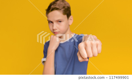Serious teen boy training box punch, focus on fist, orange studio background Serious teen boy training box punch, focus on fist, orange studio background 117499901