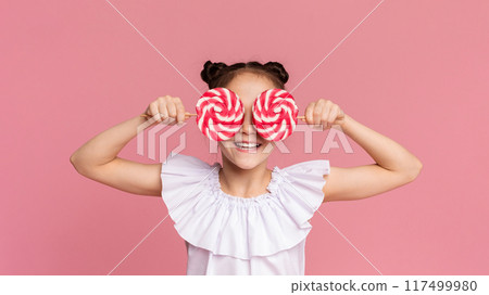 Little sweet tooth. Adorable girl covering her eyes with two colorful lollipops, pink panorama background Little sweet tooth. Adorable girl covering her eyes with two colorful lollipops, pink panorama background 117499980