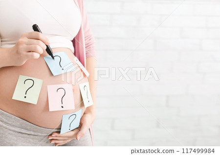 Concept of choosing baby name. Pregnant woman with question marks on paper stickers on tummy, panorama with empty space 117499984