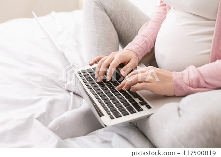 Pregnant lady using laptop, working in homeoffice or taking online education courses during maternity leave, closeup 117500019