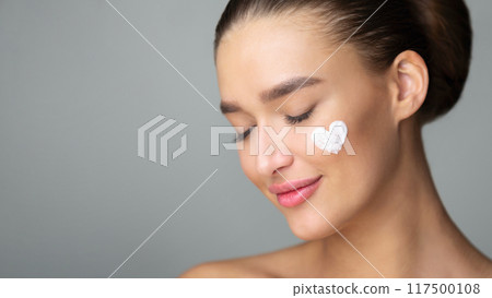 Woman with Cream In Heart Shape On Cheek, Grey Studio Background Woman with Cream In Heart Shape On Cheek, Grey Studio Background 117500108