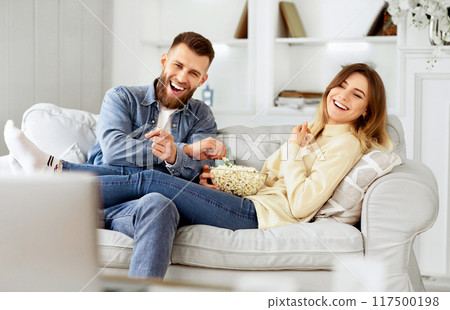 Young Couple Laughing Watching Comedy Movie Online And Eating Popcorn Young Couple Laughing Watching Comedy Movie Online And Eating Popcorn 117500198