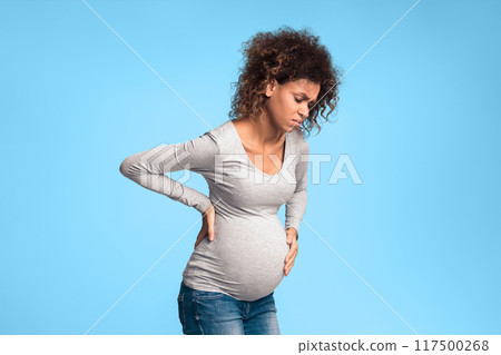 Pregnant woman suffering from abdominal and back pain, standing over gray background 117500268