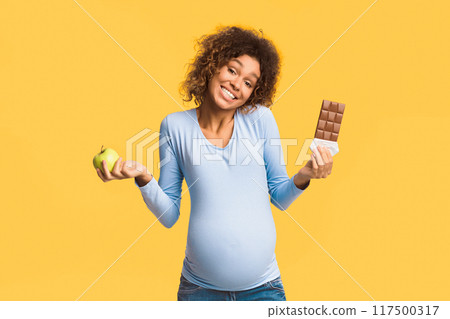 Pregnancy diet. Pregnant woman choosing between apple and chocolate over white background 117500317