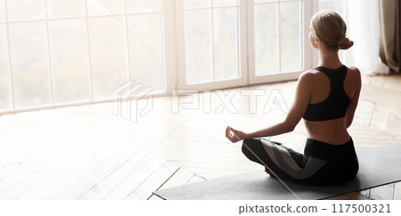 Sporty girl meditating in yoga studio, sitting in lotus pose, empty space Sporty girl meditating in yoga studio, sitting in lotus pose, empty space 117500321