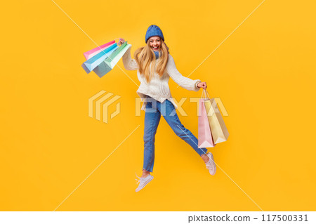 Cheerful shopaholic winter girl with purchases jumping up cause of happiness, pink background Cheerful shopaholic winter girl with purchases jumping up cause of happiness, pink background 117500331