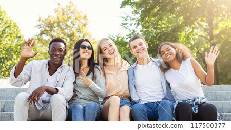 Happy friends international students spending time together in the summer city, sitting on stairs and smiling Happy friends international students spending time together in the summer city, sitting on stairs and smiling 117500377