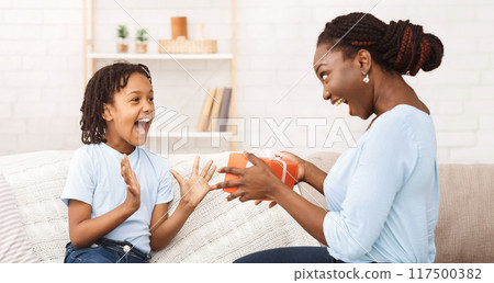 Afro Mom Making Gift For Daughter, Excited Birthday Girl With Opened Mouth Afro Mom Making Gift For Daughter, Excited Birthday Girl With Opened Mouth 117500382
