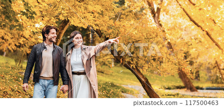 Cheerful lovers enjoying beauty of golden forest, excited girl pointing at empty space Cheerful lovers enjoying beauty of golden forest, excited girl pointing at empty space 117500463