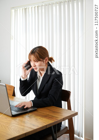 Woman talking on smartphone, suit, working from home 117500727