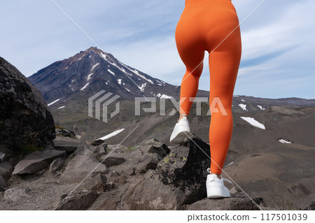 Woman in figure hugging pair of sports leggings, showcasing legs and buttocks. She has well defined gluteal, thigh musculature, engaged in outdoor fitness training in mountainous setting with volcano Woman in figure hugging pair of sports leggings, showcasing legs and buttocks. She has well defined gluteal, thigh musculature, engaged in outdoor fitness training in mountainous setting with volcano 117501039