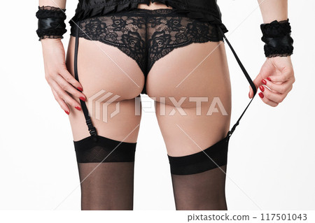 Close-up rear view of a woman's legs and buttocks, clad in panties and stockings with garters. Captivating crop view of sensuality female body, dressed in black lingerie on white background. 117501043