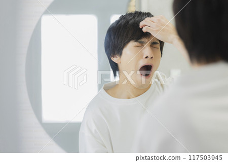 Young man looking in the mirror in the bathroom 117503945