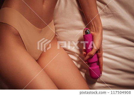 sex vibrator in the hand of a woman girl with a sexy body in panties lying on white sheet on the bed in the bedroom. Sex toys for female satisfaction and orgasm sex vibrator in the hand of a woman girl with a sexy body in panties lying on white sheet on the bed in the bedroom. Sex toys for female satisfaction and orgasm 117504908
