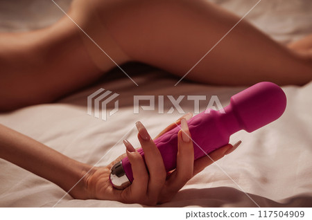 sex vibrator in hand of a woman girl with a sexy body in underwear lying on white sheet on bed in bedroom. Sex toys for female satisfaction and orgasm sex vibrator in hand of a woman girl with a sexy body in underwear lying on white sheet on bed in bedroom. Sex toys for female satisfaction and orgasm 117504909