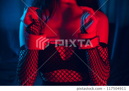 sexy submissive woman with hands in leather BDSM handcuffs. Bottom slave girl is sitting in underwear on bed. Sex with submission and domination 117504911