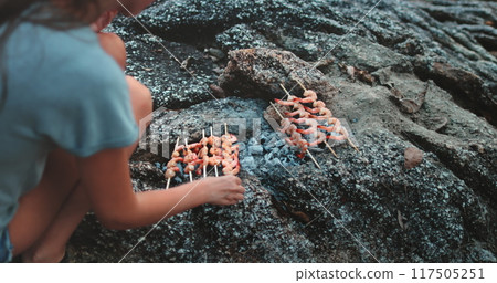 Woman is grilling shrimp skewers on a makeshift grill made of rocks in thailand. The shrimp are grilled to perfection and look delicious Woman is grilling shrimp skewers on a makeshift grill made of rocks in thailand. The shrimp are grilled to perfection and look delicious 117505251