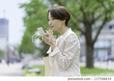 Middle-aged woman fixing her lipstick in the park Middle-aged woman fixing her lipstick in the park 117506634