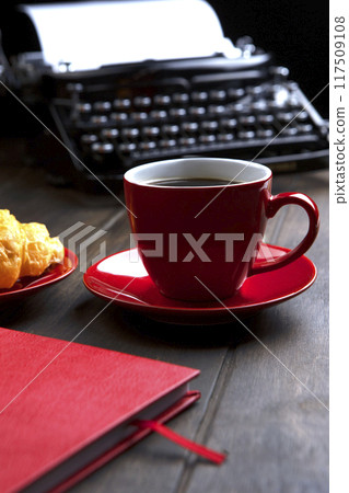 A red cup with coffee. An old vintage typewriter and an empty piece of paper. The notebook is red. The concept of a business breakfast. 117509108