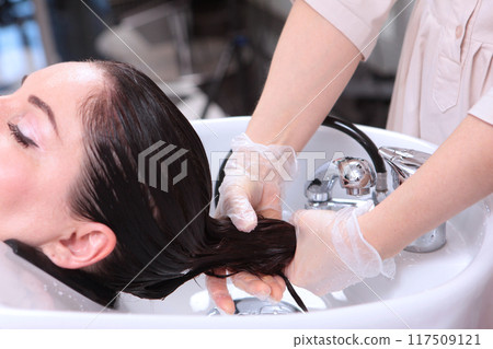In beauty salon, strengthening mask is applied to hair. Wet hair. Mask for moisturizing hair.Long hair is washed and moisturized with cosmetic mask. In beauty salon, strengthening mask is applied to hair. Wet hair. Mask for moisturizing hair.Long hair is washed and moisturized with cosmetic mask. 117509121