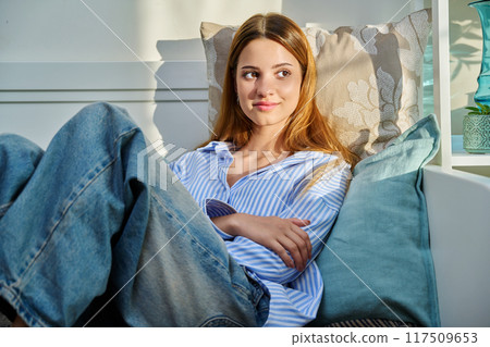 Young woman using smartphone sitting on couch at home Young woman using smartphone sitting on couch at home 117509653