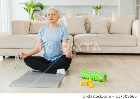 Yoga mindfulness meditation. Senior adult mature woman practicing yoga at home. Mid age old lady sitting in lotus pose on yoga mat meditating relaxing. Older middle aged woman doing breathing practice 117509666
