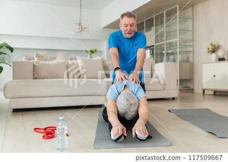Fitness workout training. Senior adult mature healthy fit couple doing sports exercise on yoga mat at home. Mid age old man trainer helping woman stretching training. Health care healthy lifestyle Fitness workout training. Senior adult mature healthy fit couple doing sports exercise on yoga mat at home. Mid age old man trainer helping woman stretching training. Health care healthy lifestyle 117509667