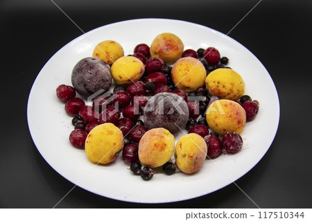 A Berry mix from frozen currant, apricot, plum, cherry on the white plate. Frozen Berries from freezer. A background with frozen plum, currant, apricot and cherry. A healthy Berries on the background 117510344