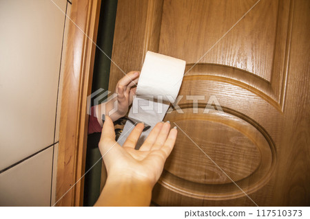 A girl is asking a toilet paper in the toilet. A Hand gives toilet paper A girl is asking a toilet paper in the toilet. A Hand gives toilet paper 117510373