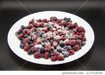 A Berry mix in sugar from frozen raspberries and blueberries on the white plate. A Frozen Berries with Sugar. A sweet background with frozen raspberries and blueberries A Berry mix in sugar from frozen raspberries and blueberries on the white plate. A Frozen Berries with Sugar. A sweet background with frozen raspberries and blueberries 117510384