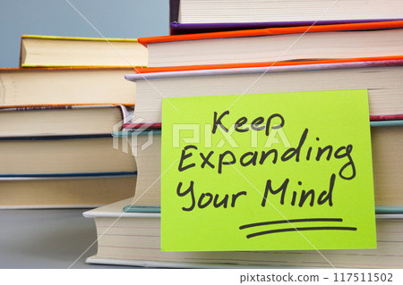 Stack of books and a note with the phrase Keep expanding your mind. Continuous learning and personal growth. 117511502