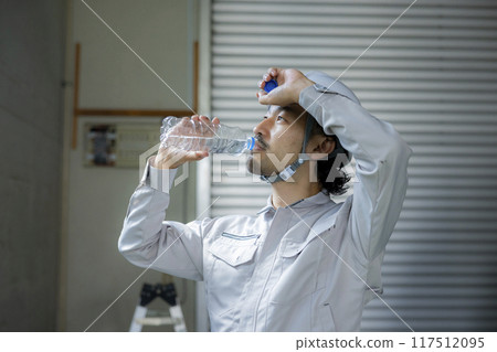 A man in work clothes drinking water 117512095