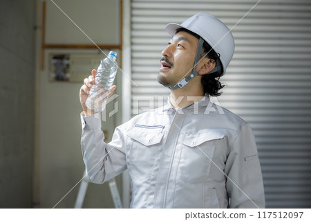 A man in work clothes drinking water 117512097