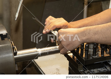 Close up scene the machine operator measuring dimension of metal shaft parts by Vernier caliper on lathe machine. Close up scene the machine operator measuring dimension of metal shaft parts by Vernier caliper on lathe machine. 117514006