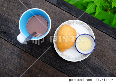 Yang fried dumpling or Bread fried bun recipe with sweetened condensed milk in a bowl and a cup of hot chocolate on wooden table in tropical garden. Asain Breakfast in Thailand Yang fried dumpling or Bread fried bun recipe with sweetened condensed milk in a bowl and a cup of hot chocolate on wooden table in tropical garden. Asain Breakfast in Thailand 117514286