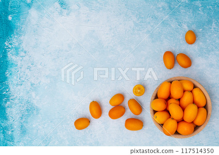 Kumquat in a wooden bowl on a blue background. Kumquat in a wooden bowl on a blue background. 117514350