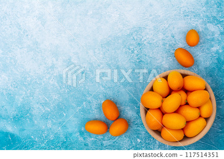 Kumquat in a wooden bowl on a blue background. 117514351
