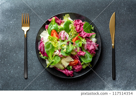 Salad with cabbage, radicchio and tomatoes in black plate on dark background 117514354