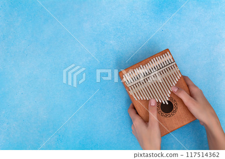 Female hands with a kalimba on a blue background Female hands with a kalimba on a blue background 117514362