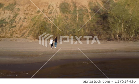Young couple in love walking on the beach and spinning holding hands. Aerial view of the beach. 4k 117514430