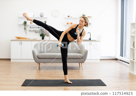 Woman exercising at home with dumbbells performing kick Woman exercising at home with dumbbells performing kick 117514923