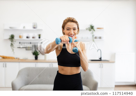 Smiling woman exercising at home with dumbbells in bright room Smiling woman exercising at home with dumbbells in bright room 117514940