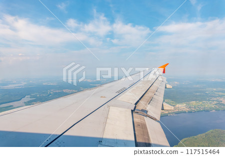 View of airplane wing, blue skies and green land during landing. Airplane window view. 117515464