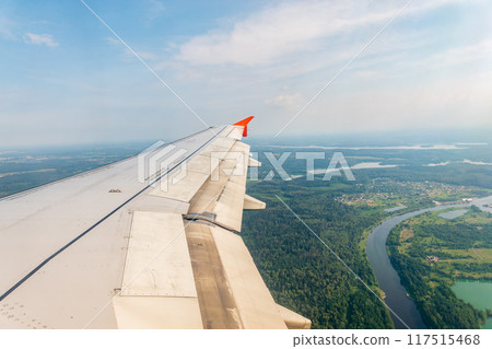 View of airplane wing, blue skies and green land during landing. Airplane window view. 117515468
