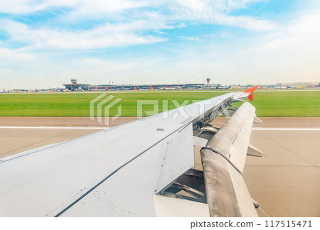 View of airplane wing, blue skies and green land during landing. Airplane window view. 117515471