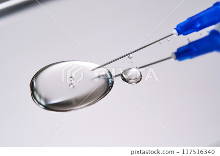 A drop of medicine flowing from a syringe with a needle. 117516340
