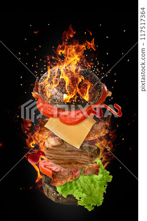 Cheeseburger with a piece of meat, tomato, green lettuce and a bun with sesame seeds on a black background with fire Cheeseburger with a piece of meat, tomato, green lettuce and a bun with sesame seeds on a black background with fire 117517364