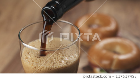stout beer poring into glass with bagels on background 117517455